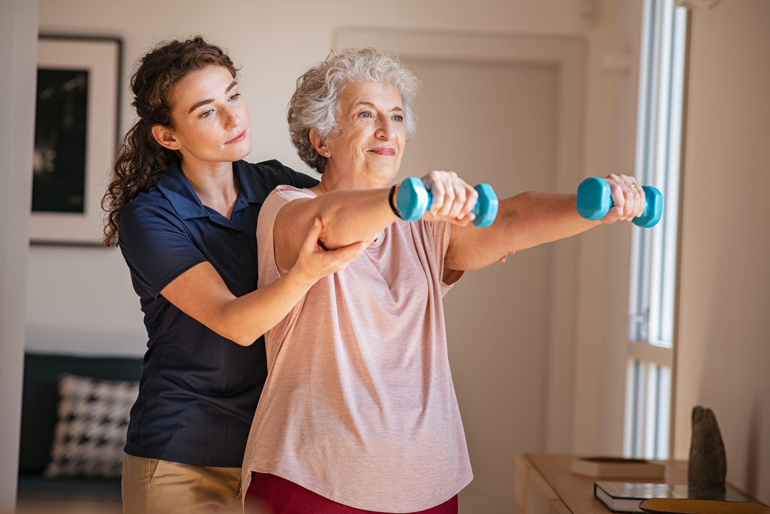Old,Woman,Training,With,Physiotherapist,Using,Dumbbells,At,Home.,Therapist